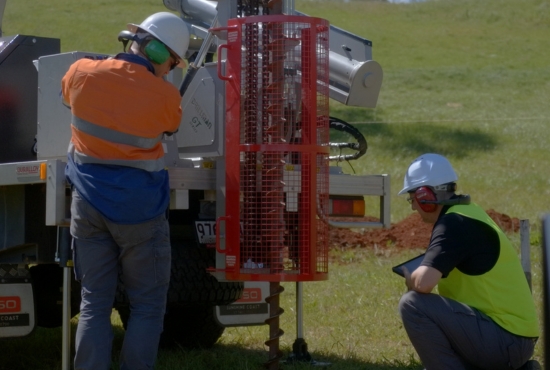 A geotechnical operating a vehicle-mounted auger to drill a borehole and retrieve a core sample while a geotechnical engineer supervises