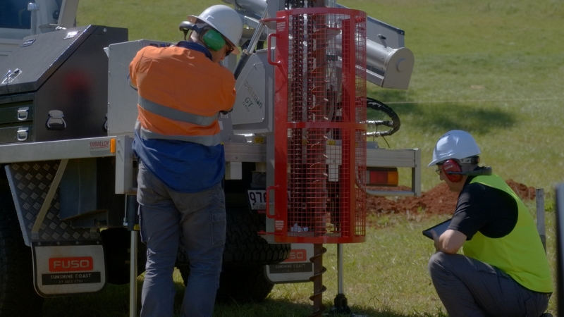 A geotechnical operating a vehicle-mounted auger to drill a borehole and retrieve a core sample while a geotechnical engineer supervises